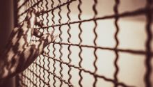 Hands on a wire-mesh prison enclosure to illustrate the article Is Purgatory Biblical?