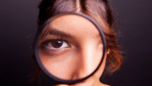 Photo of a girl looking through a magnifying glass at the camera, to illustrate the article Why We Need Spiritual Discernment Now More Than Ever